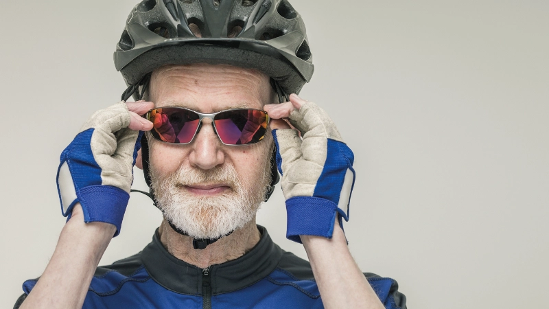 Un senior portant un casque et des lunettes de cycliste regarde la caméra.