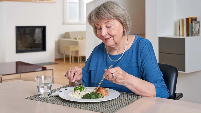Une personne âgée est assise à table et mange son repas.