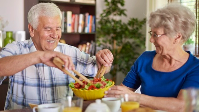 Un couple âgé: elle tient le saladier, il se sert de la salade.