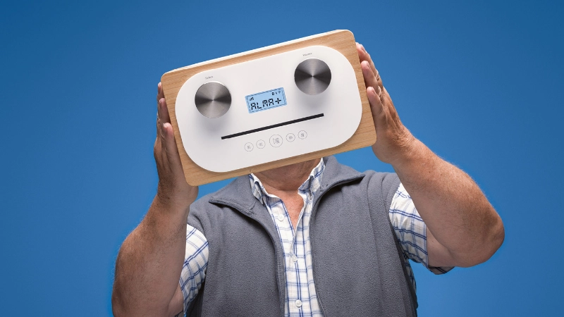 Un homme âgé tient sa radio DAB dans ses mains devant son visage (Droits d'image: Office fédéral de la communication OFCOM).