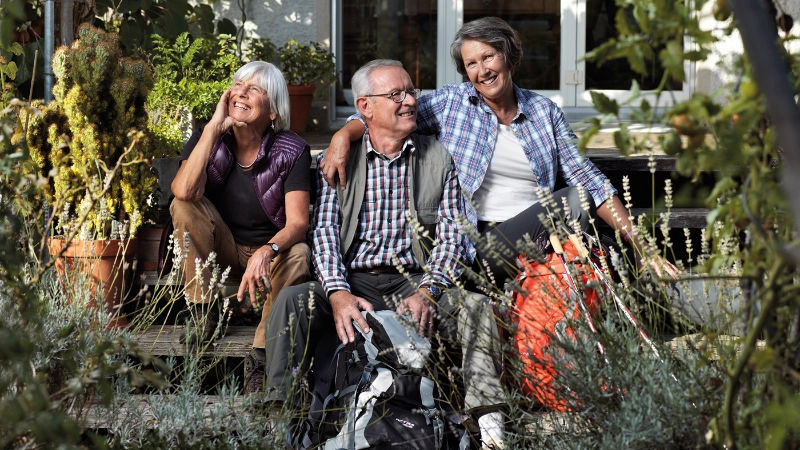 Trois seniors sont assis dans le jardin sur un escalier et rient